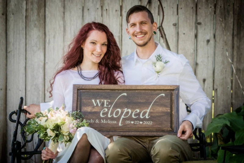 Eloped couple on bench holding 'We Eloped' sign, beaming with joy – Imaginarium Pictures wedding photography